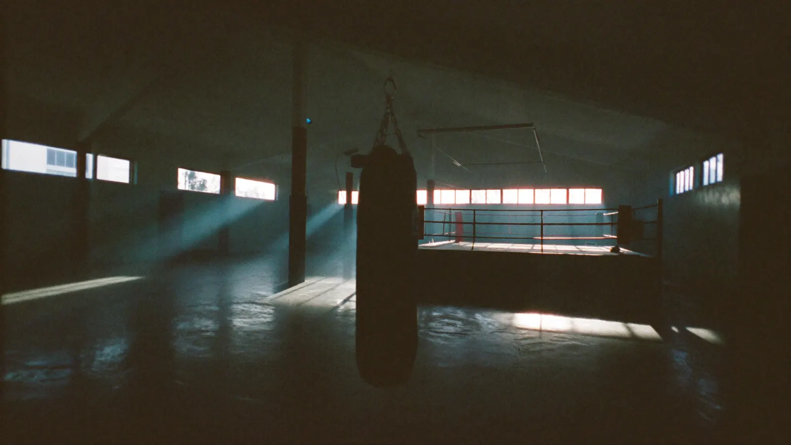 Gimnasio de boxeo vacío con una bolsa pesada y un ring de cuerdas rojas
